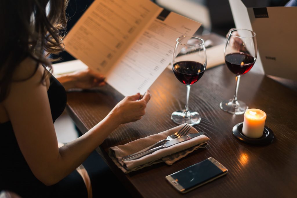 Foto di donna che guarda il menù e beve vino