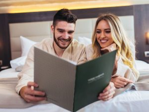 Foto di coppia sdraiata sul letto che sfoglia il menu dell'hotel